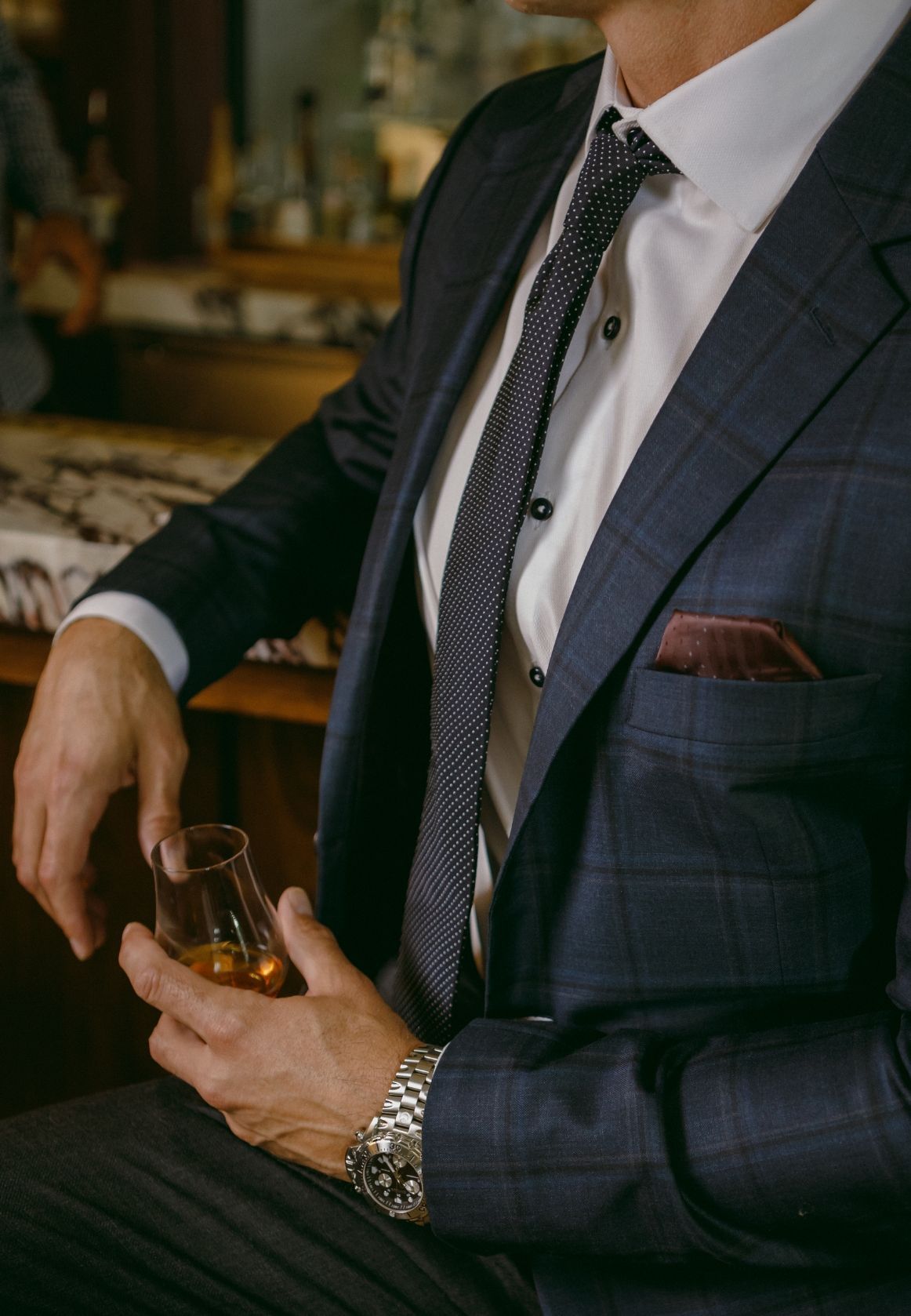A man in a suit and tie is holding a glass of whiskey.