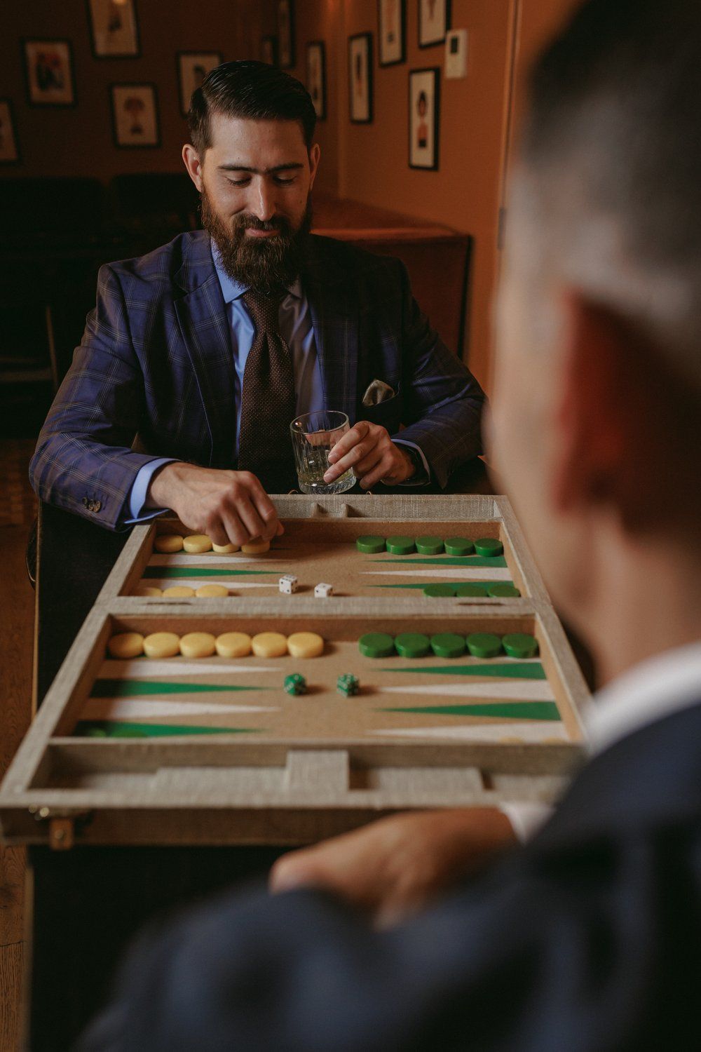 A man in a suit and tie is playing a game of backgammon with another man.