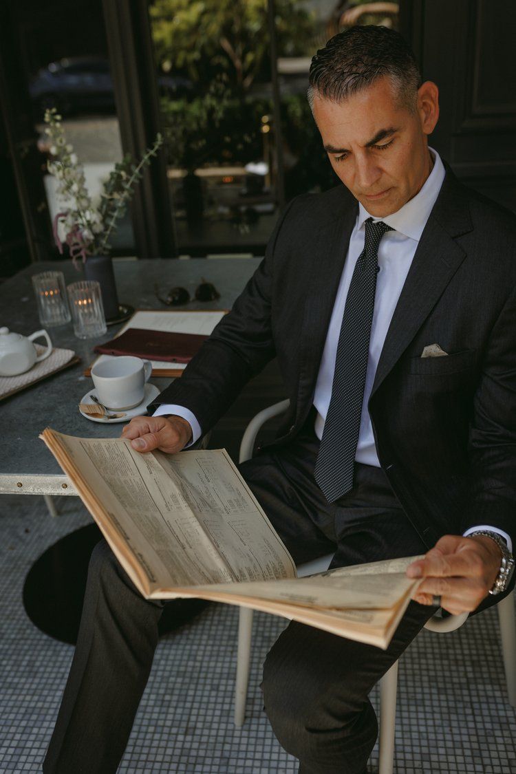 A man in a suit and tie is sitting at a table reading a book.