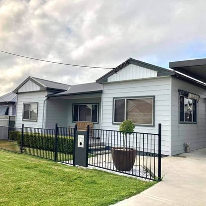 A white house with a black fence and a potted plant in front of it — Heritage Window Awnings in the Hunter Valley, NSW