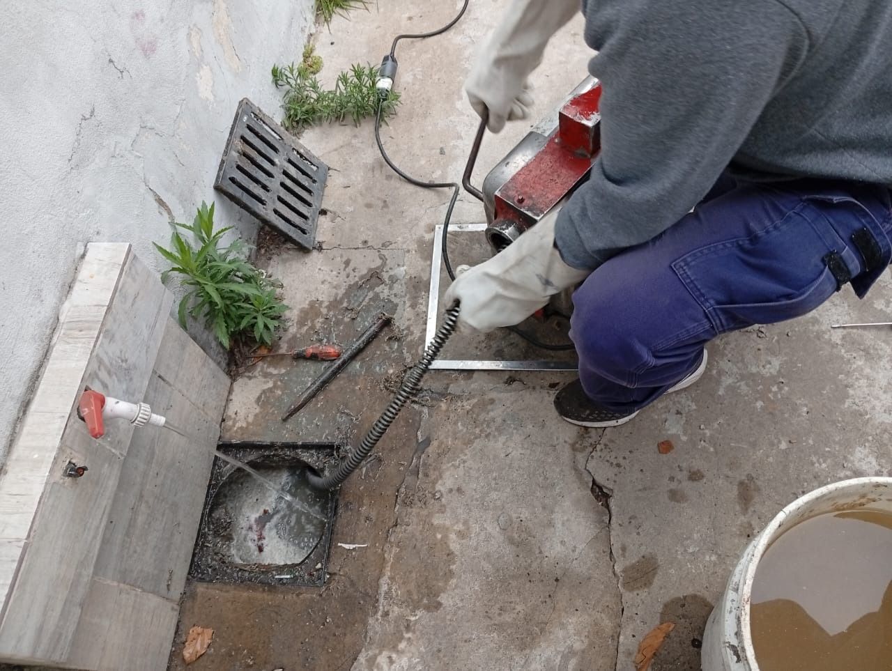 Un trabajador utiliza una sierra eléctrica para cortar hormigón junto a un desagüe en una zona de reparaciones al aire libre.