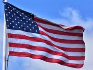 An american flag is waving in the wind against a blue sky