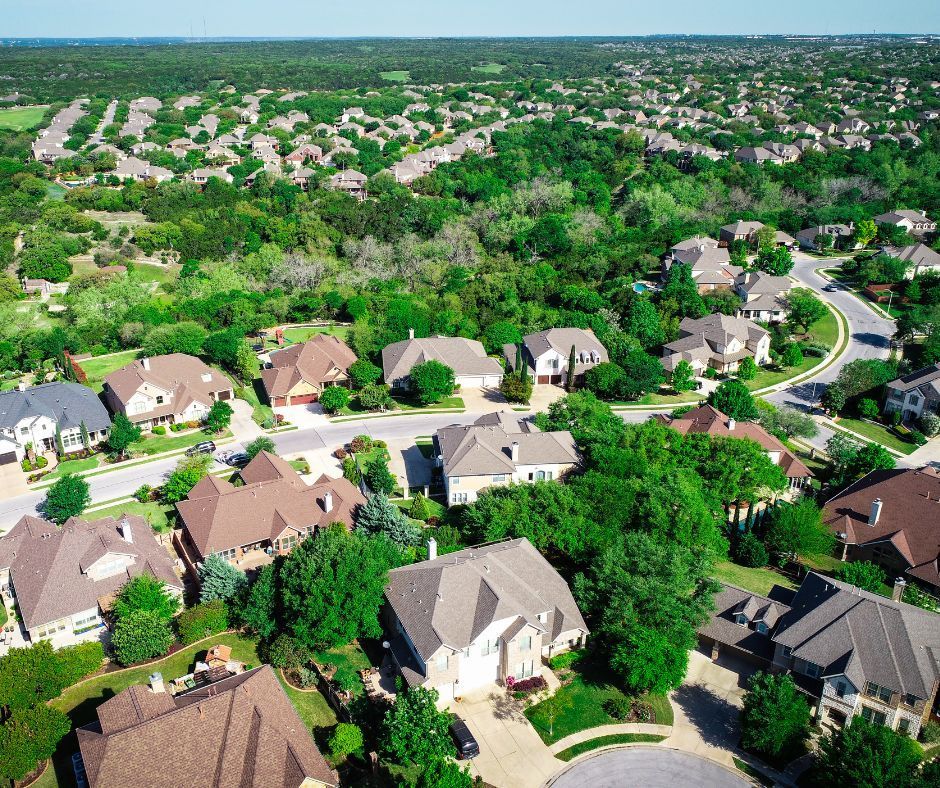 Aerial view of a suburban neighborhood with houses and green trees under a clear blue sky.