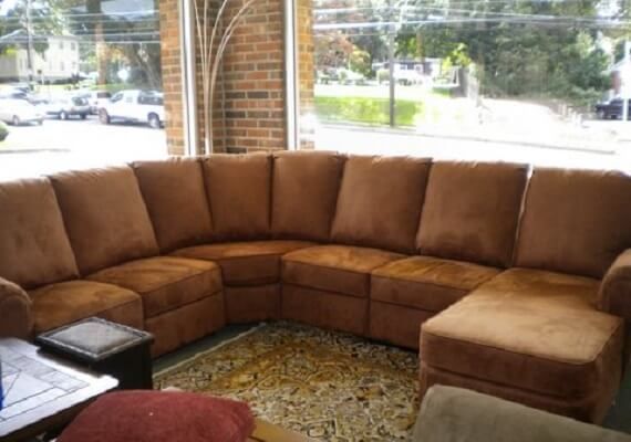 A brown sectional couch is in a living room next to a window