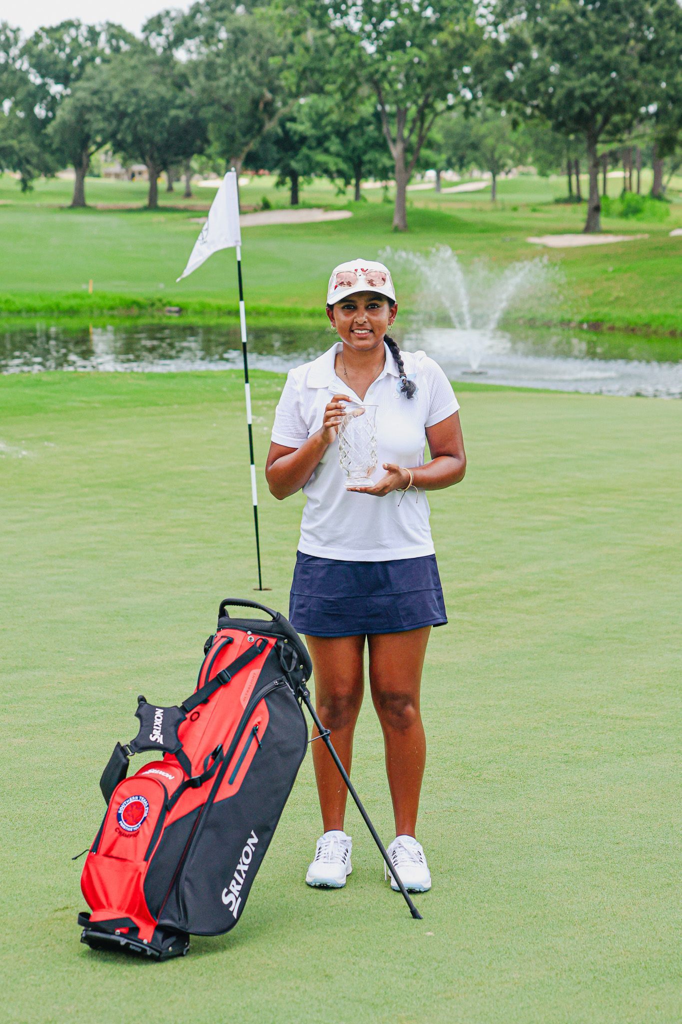 A young man is standing on a golf course holding a trophy and a golf bag.