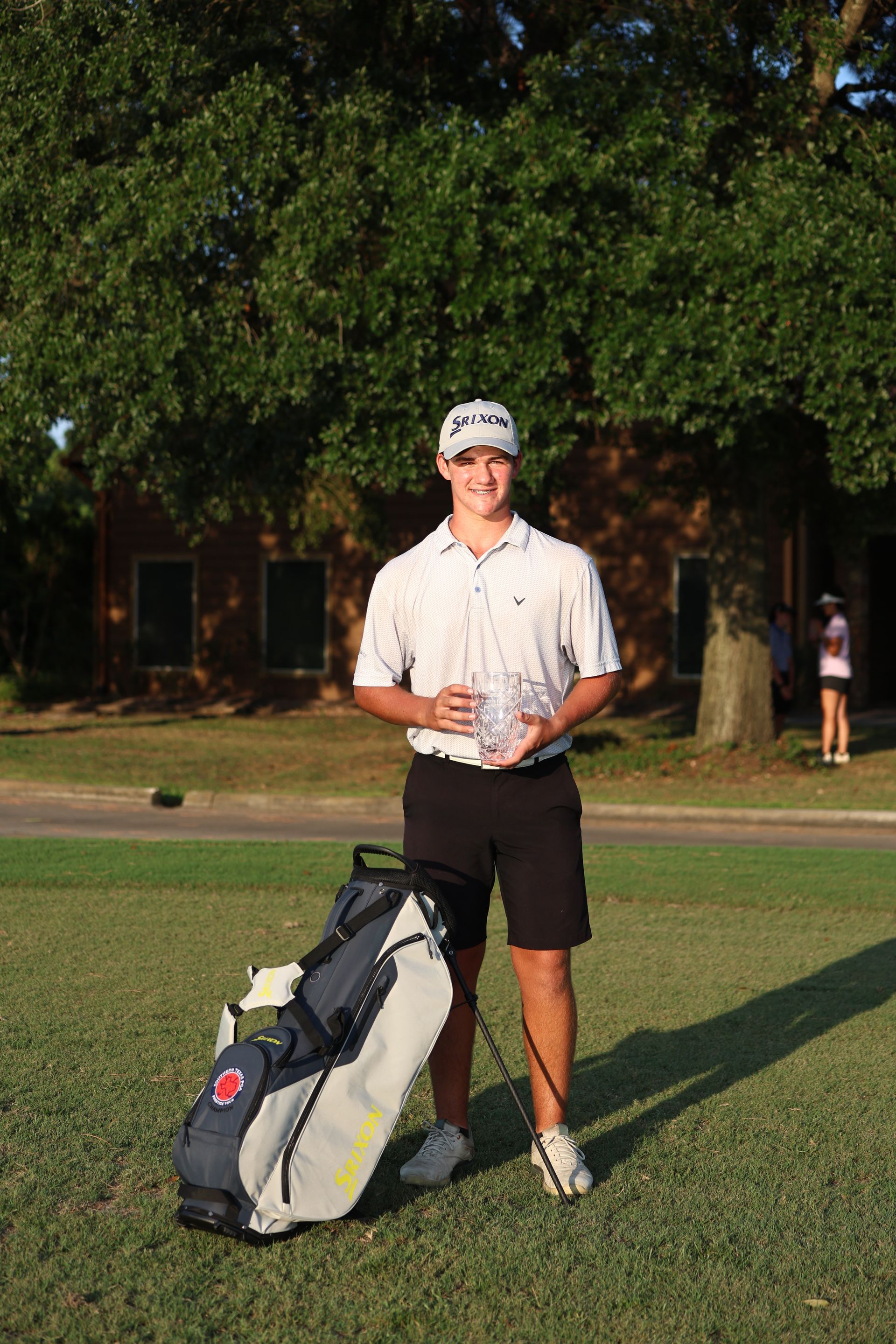 A woman is standing on a golf course with a golf bag.