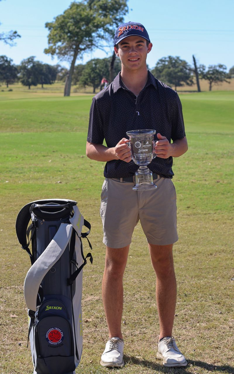 Young woman golfer in pink shirt and black shorts stands next to golf bag on a green course.