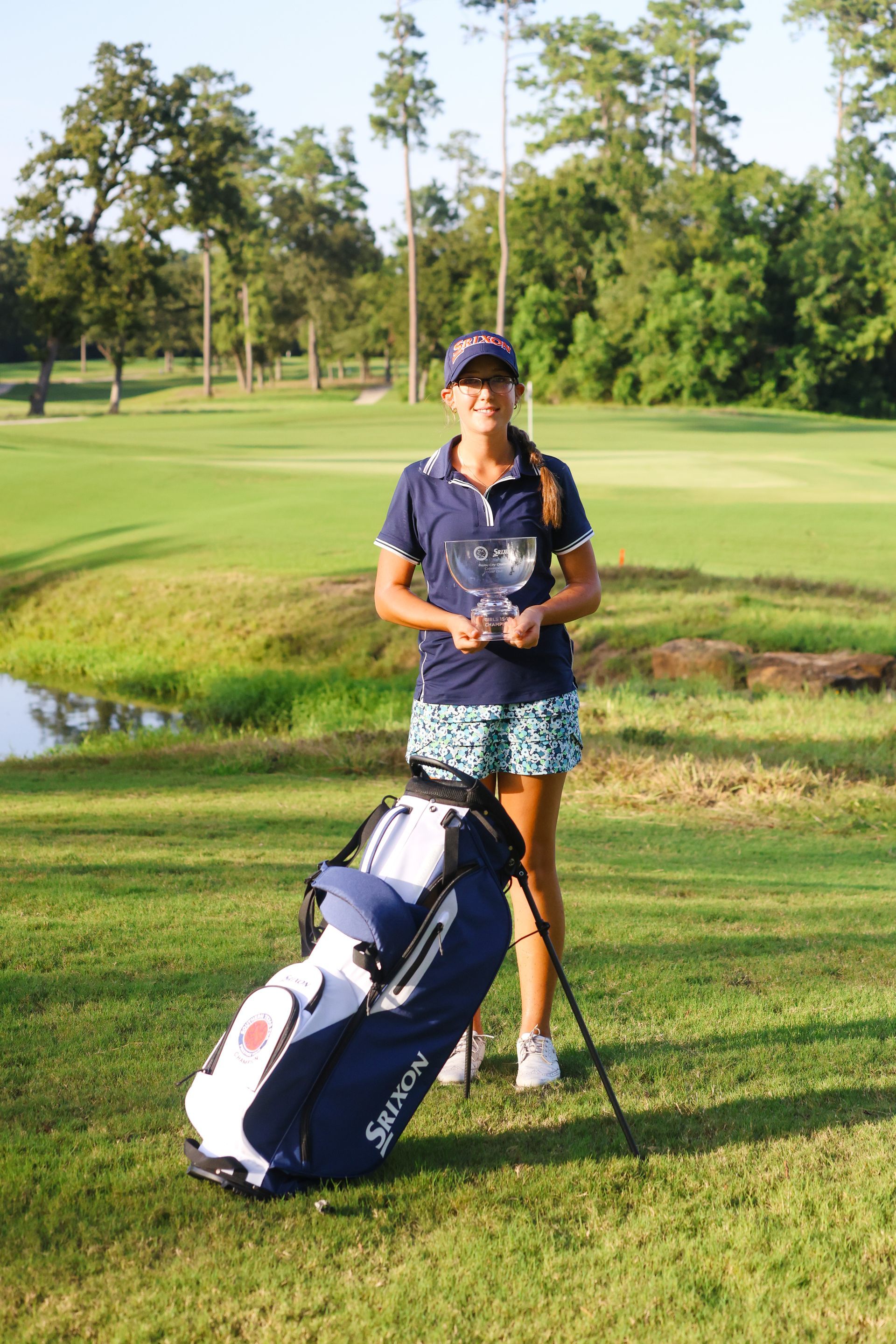 A woman is standing on a golf course with a golf bag.