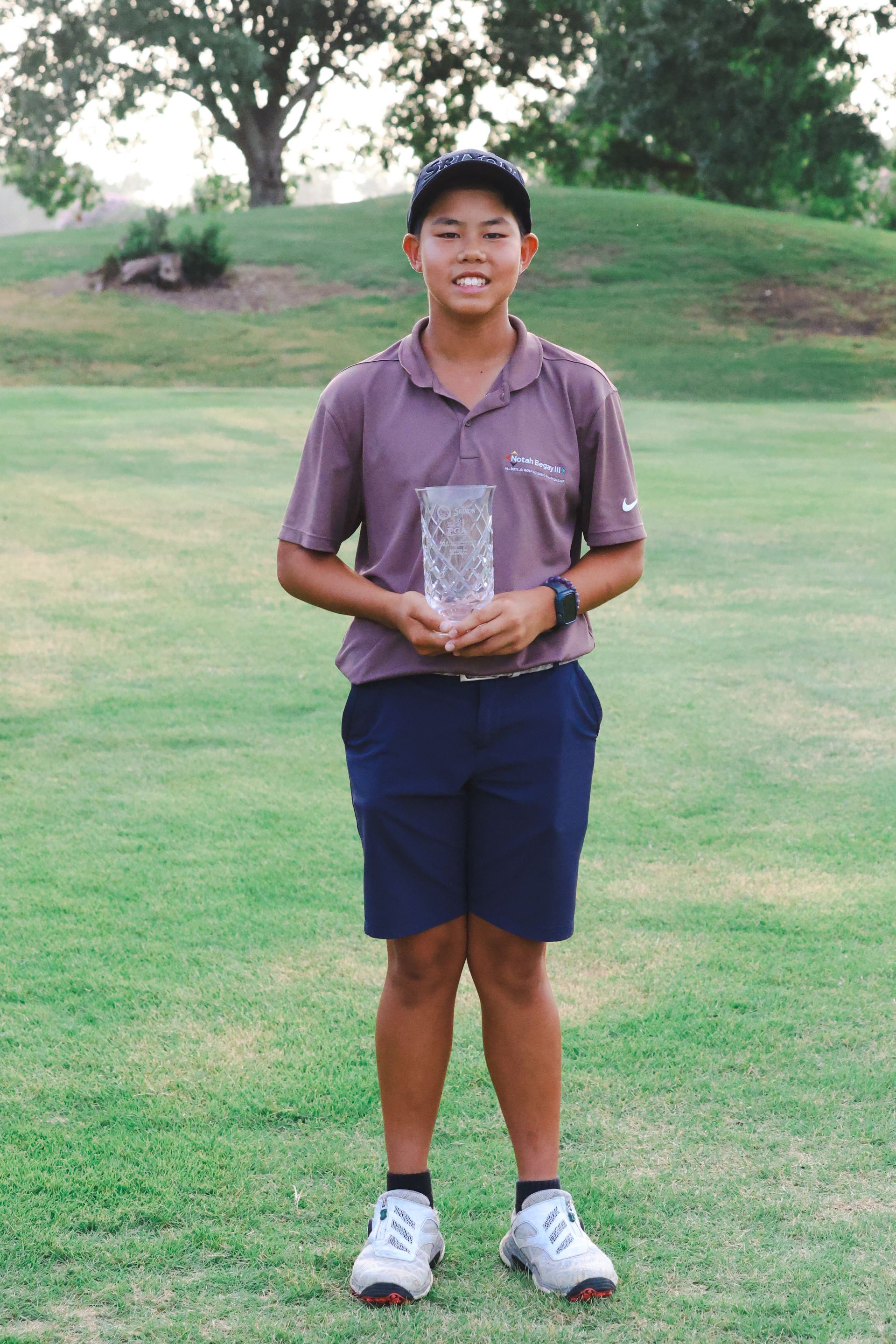 A woman is standing next to a golf bag on a golf course holding a trophy.