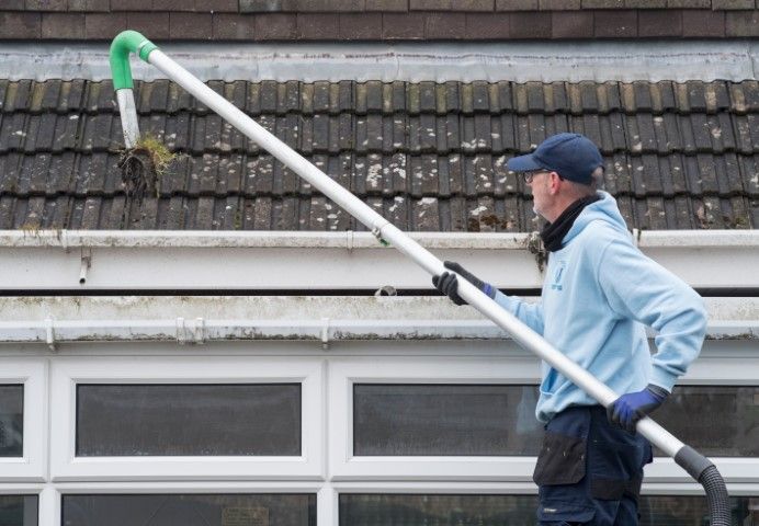 Worker using a long pole to clean a roof gutter on a building exterior