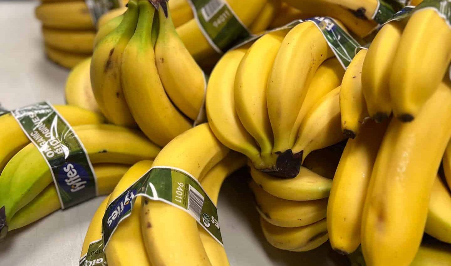 Bunches of yellow bananas, some wrapped with green labels, stacked together.