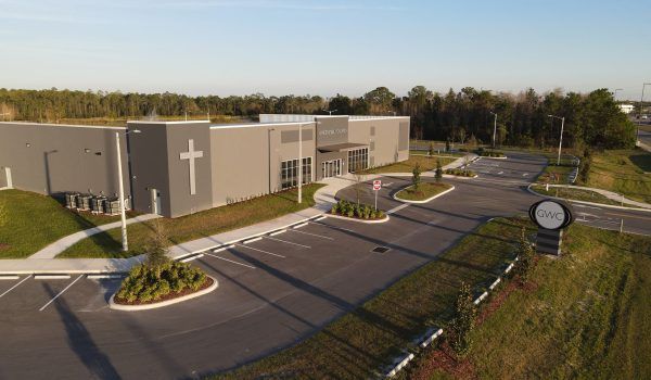 Exterior view of a modern gray church with a cross on the side and a sign in the foreground.