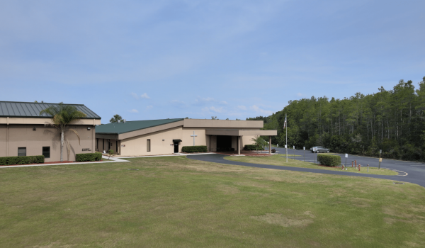 Building with green roof and landscaping, sunny day with cars and trees in the distance.