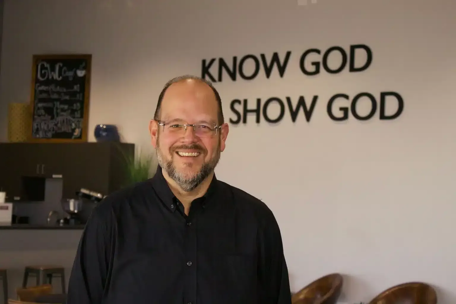 Man smiles in front of a wall with text 