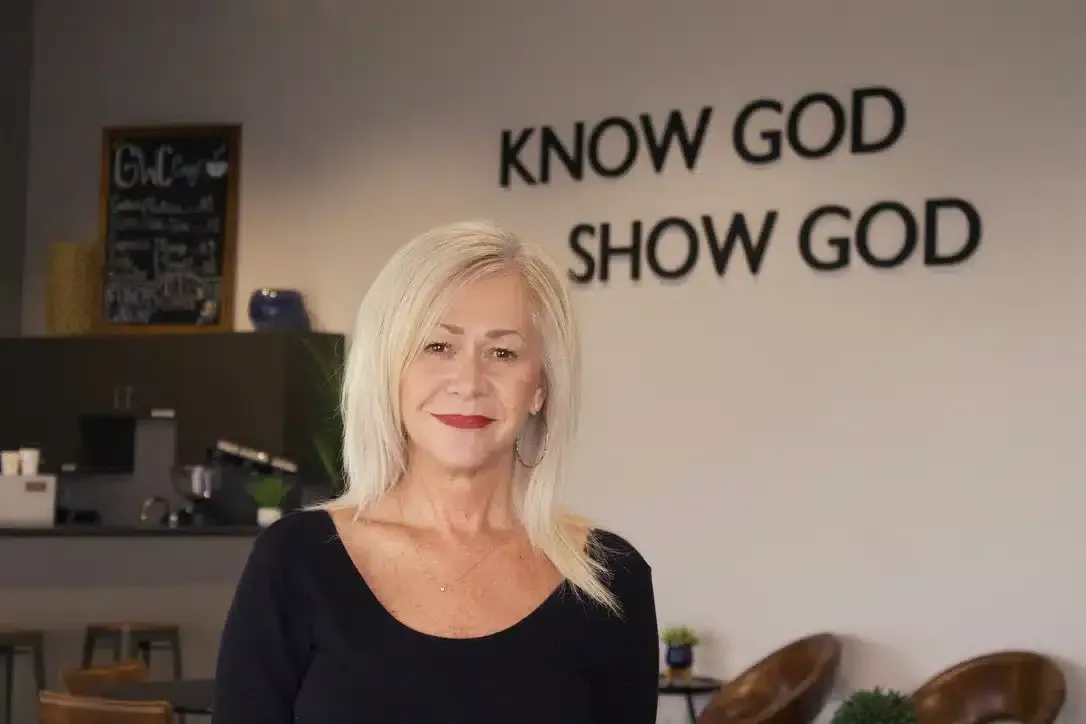 Woman in a black top stands in front of a wall that reads 