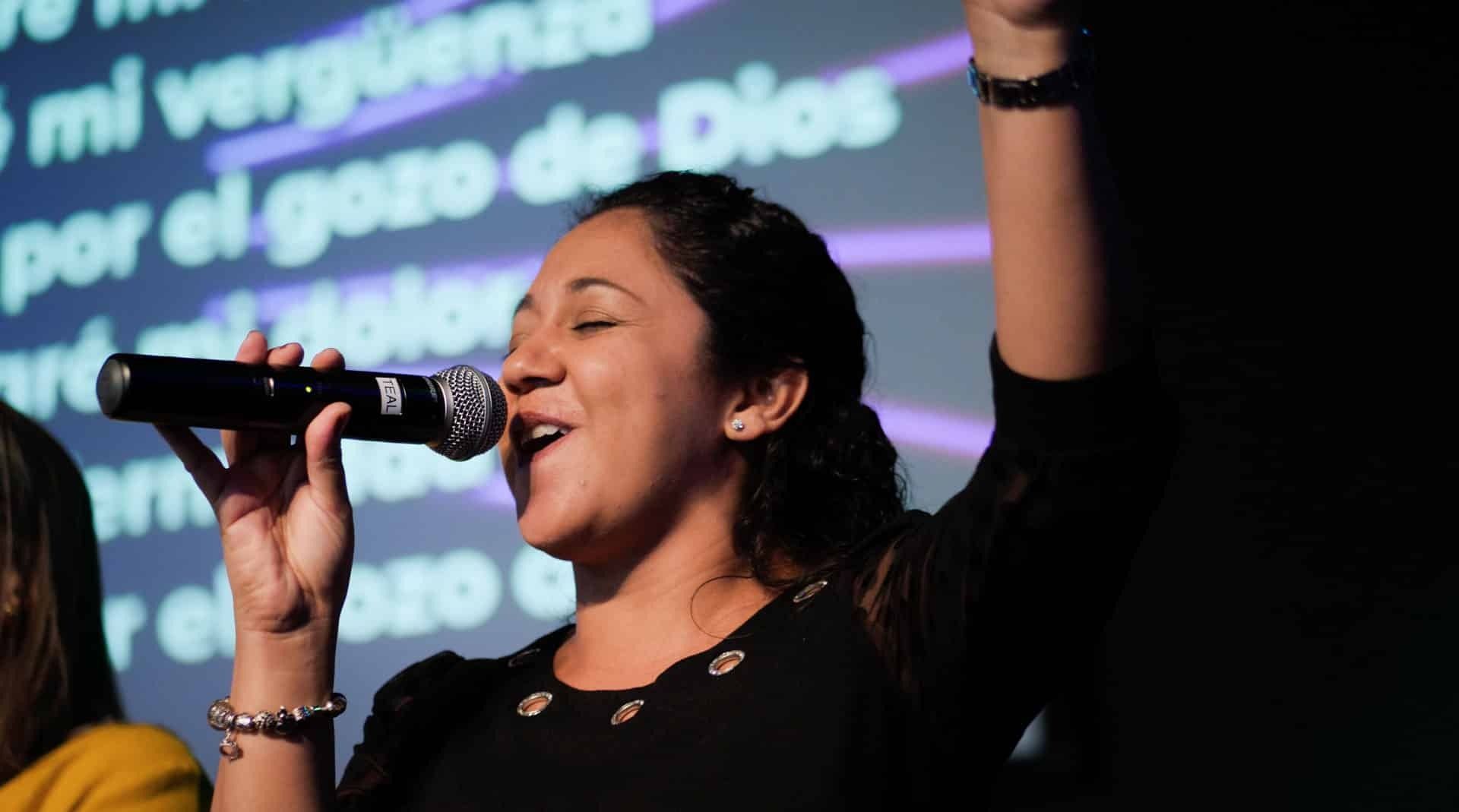 Woman singing into a microphone with her arm raised, text in the background.