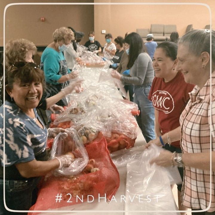 Volunteers at tables packing food into bags, smiling. Tag: #2NDHARVEST.
