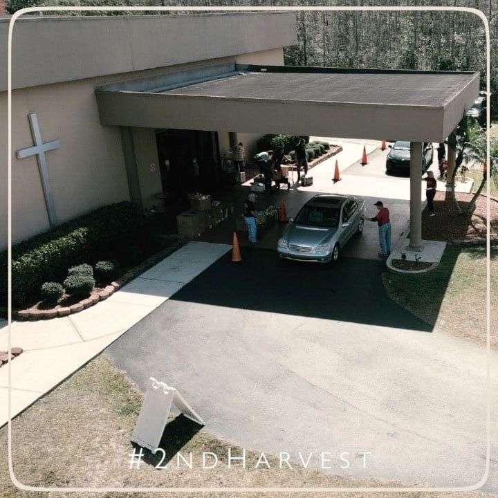 Church with cars and people unloading items, likely food, from a distribution event.