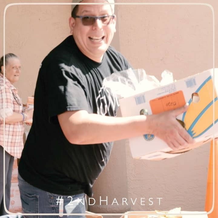 Man smiling, carrying a box of food at an outdoor distribution event.