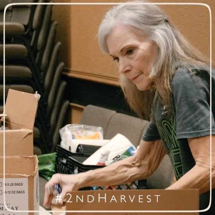 Woman packing boxes with supplies, likely for a food bank. She is focused, in a room with stacked chairs.