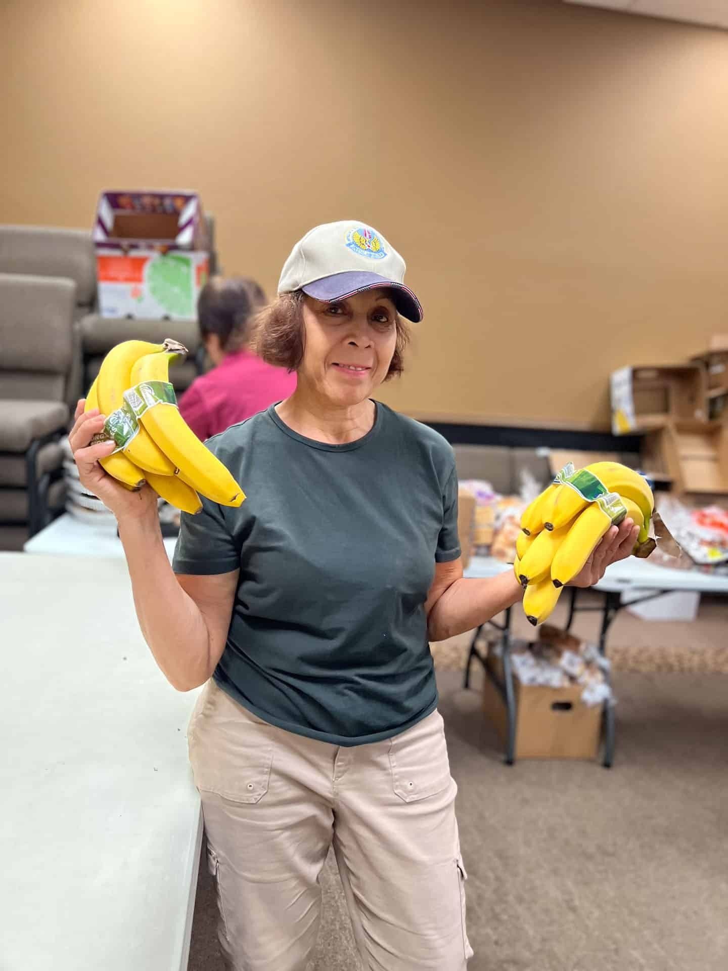 Woman holding two bunches of ripe bananas indoors; preparing food.