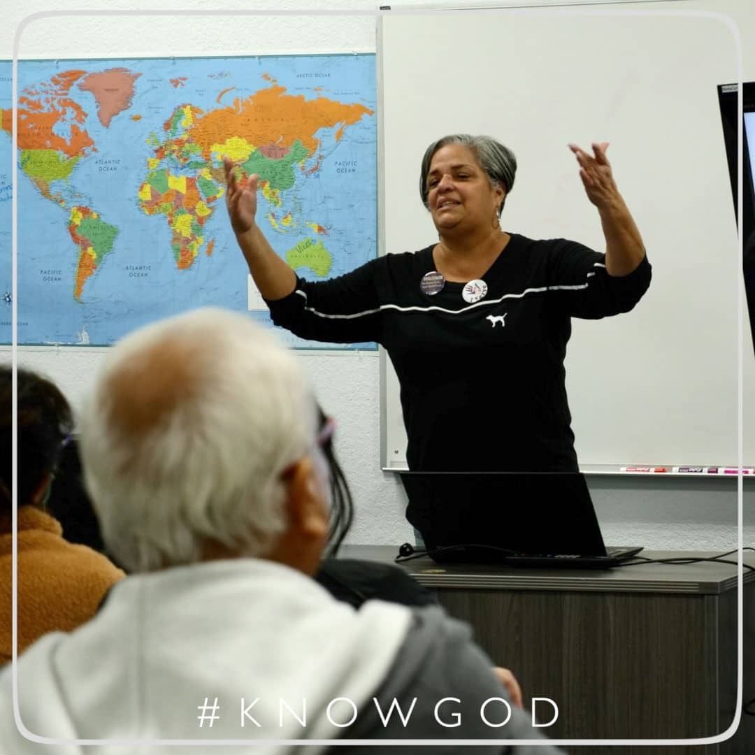 Woman speaking with arms raised in front of a world map and audience.