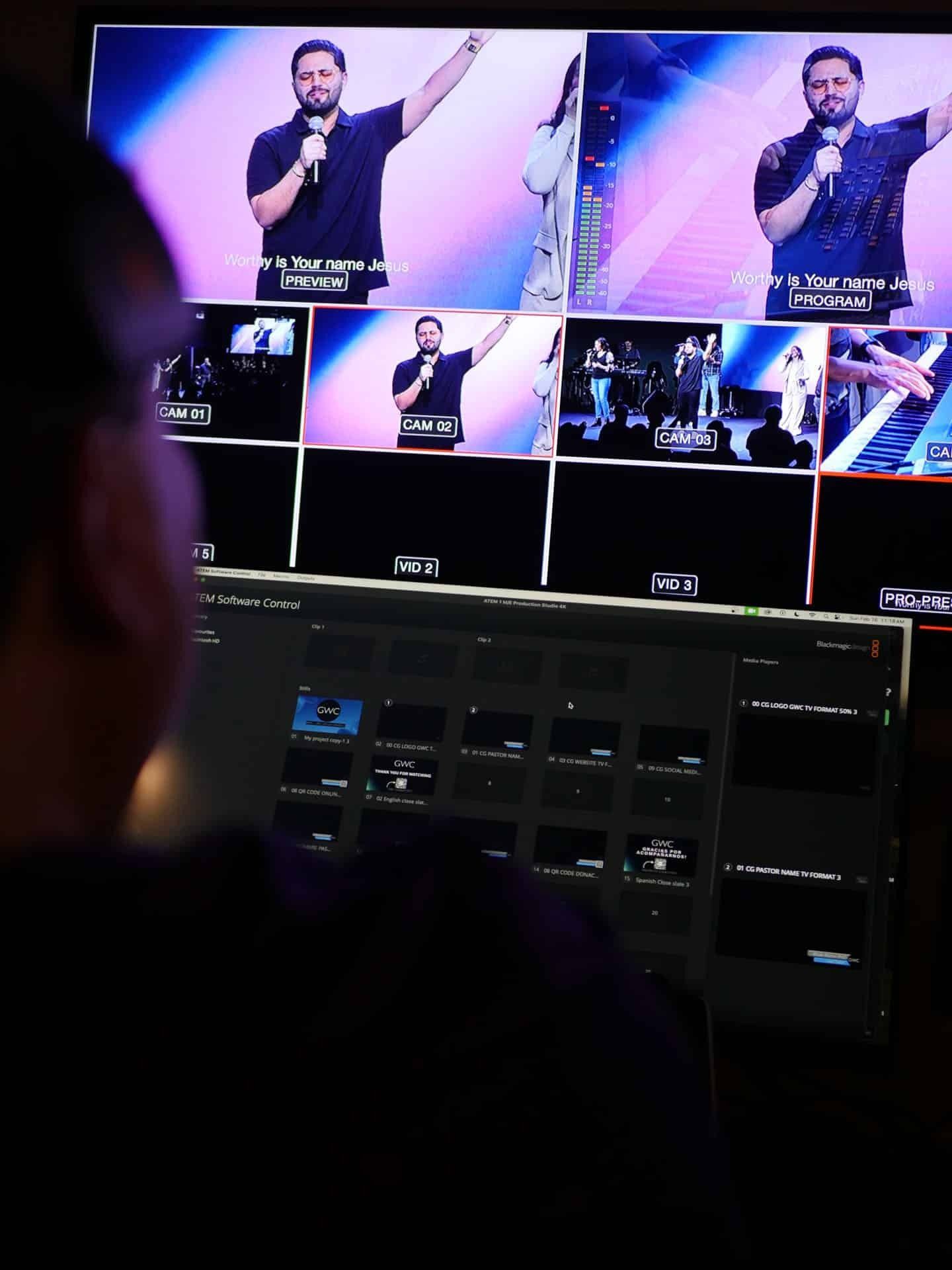 Person operating a video production control panel, viewing a monitor with live feed and camera previews.