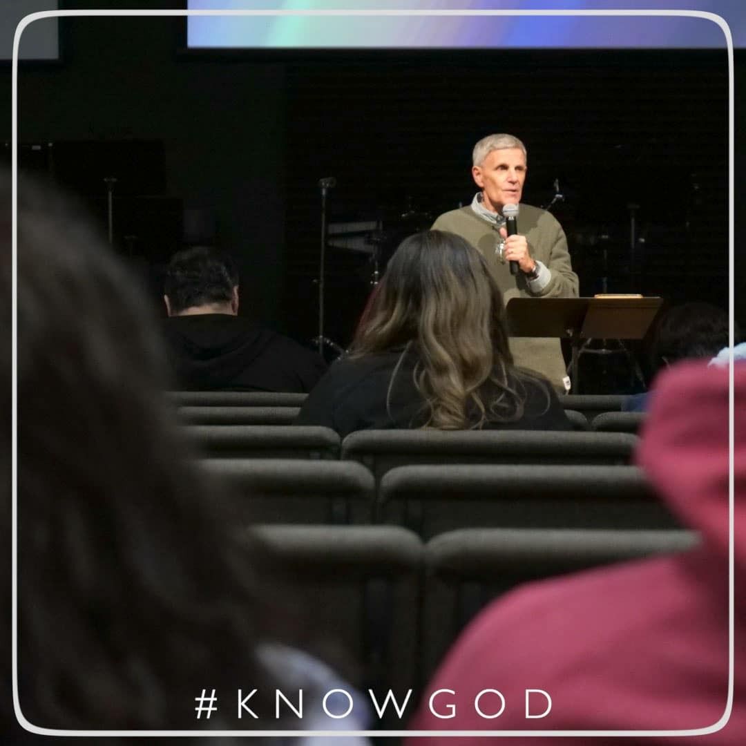 Man speaking from a podium at a church, addressing an audience. A screen is behind him. 