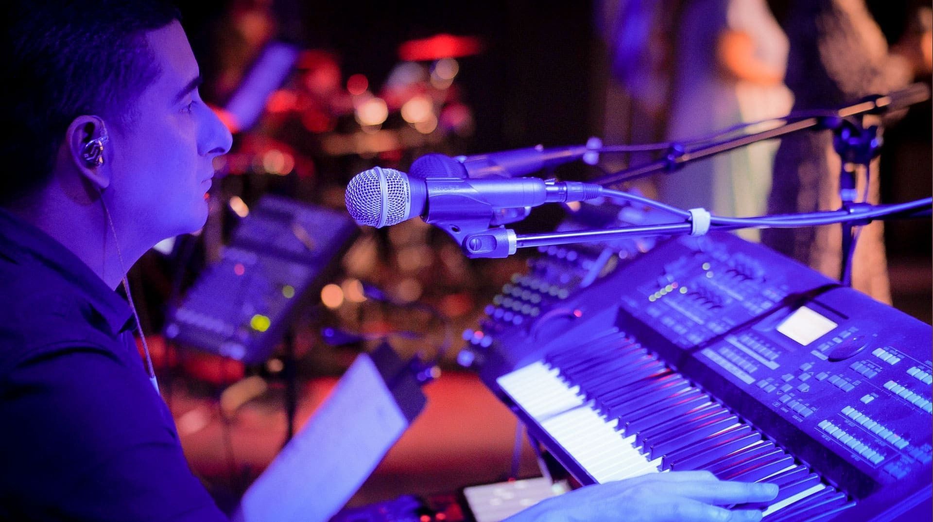 Man singing into a microphone, playing a synthesizer onstage with blue stage lighting.