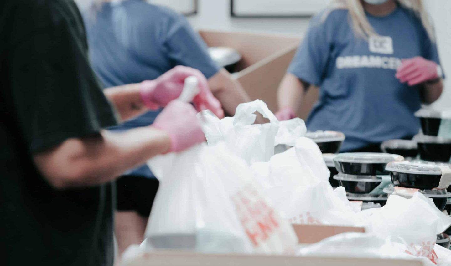 People in a room packing meals in bags, wearing gloves.