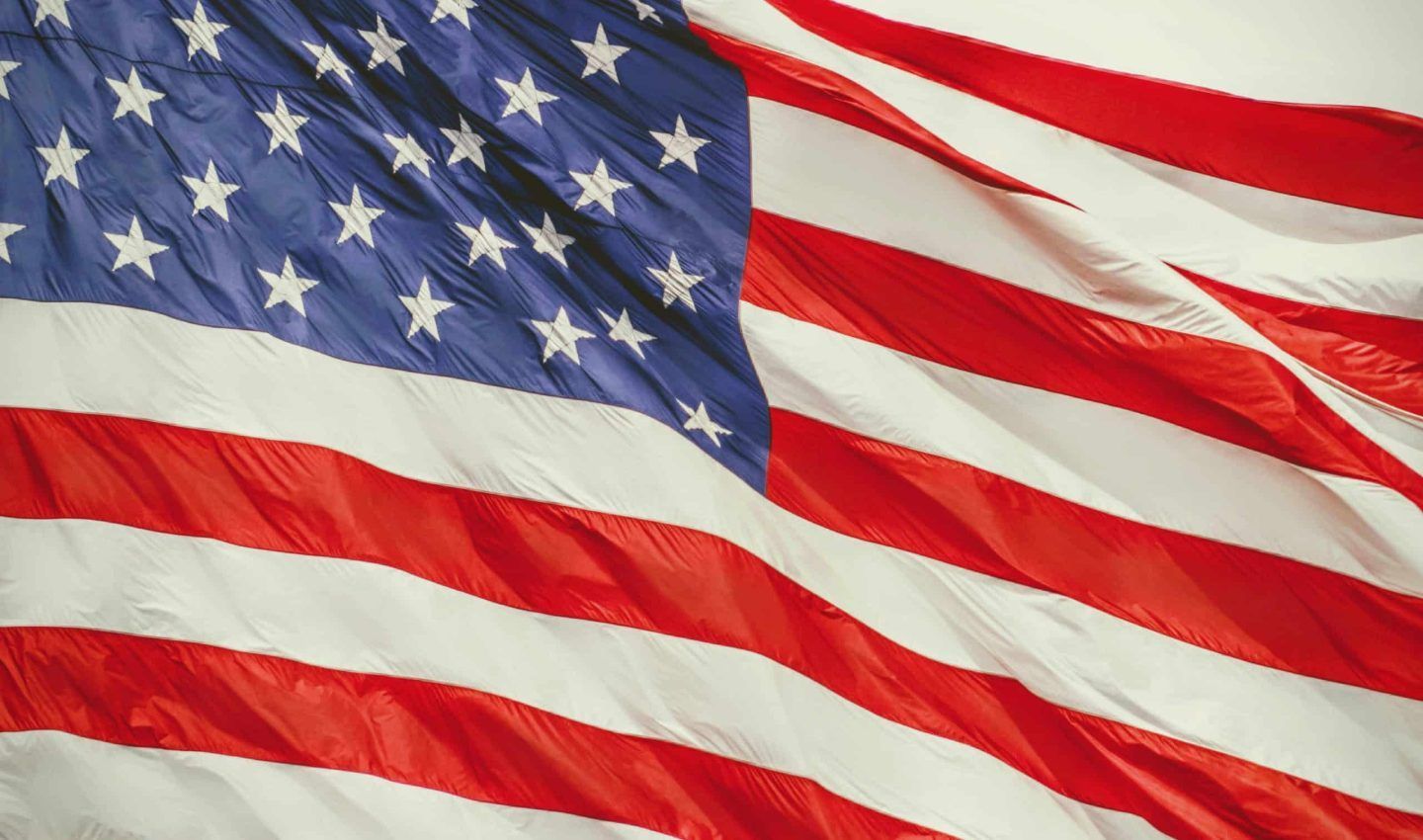 American flag waving in the wind, with red and white stripes and blue field of stars.