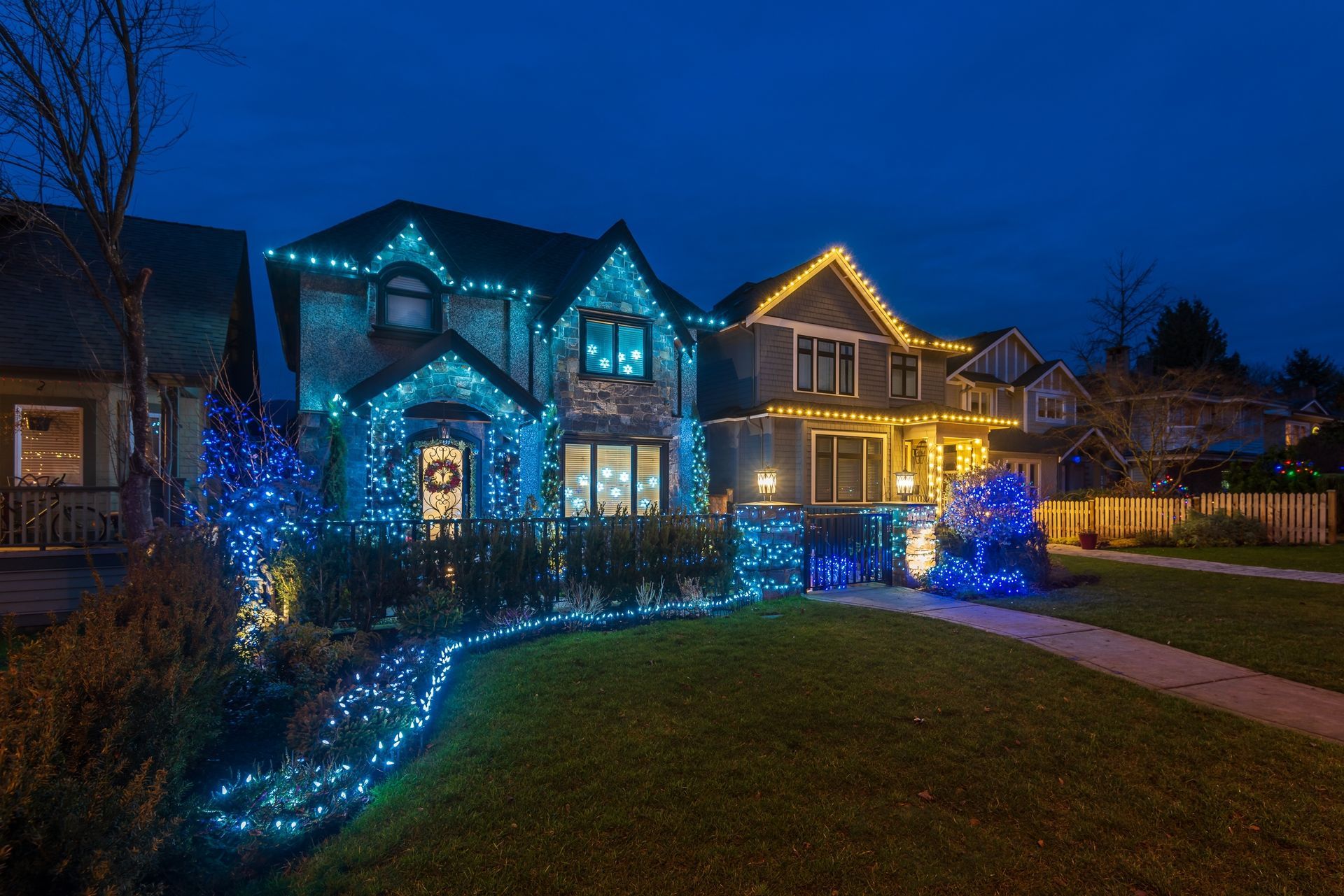 Houses decorated with blue and gold Christmas lights against a dark blue evening sky.
