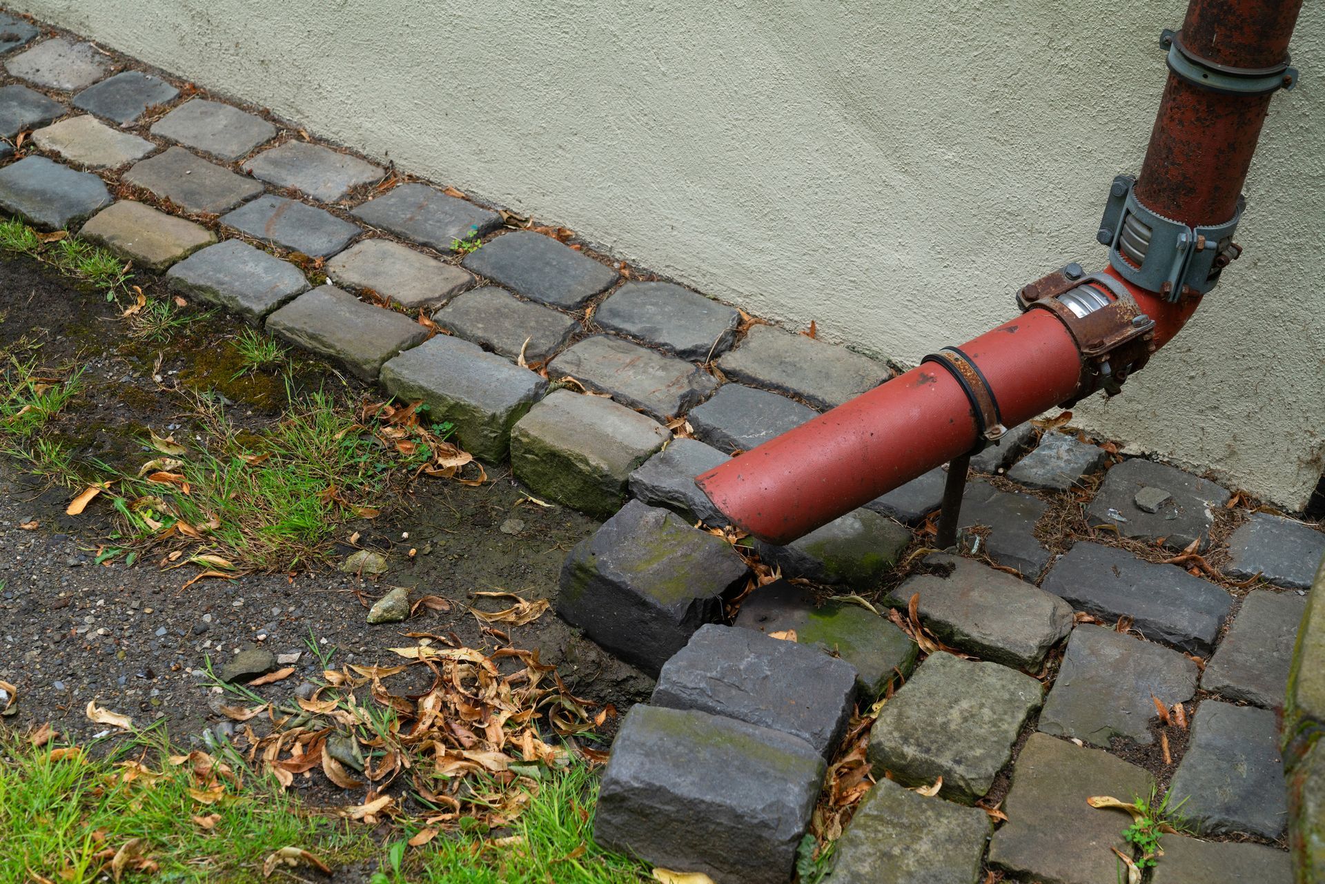 A red pipe is sitting on a sidewalk next to a brick walkway.