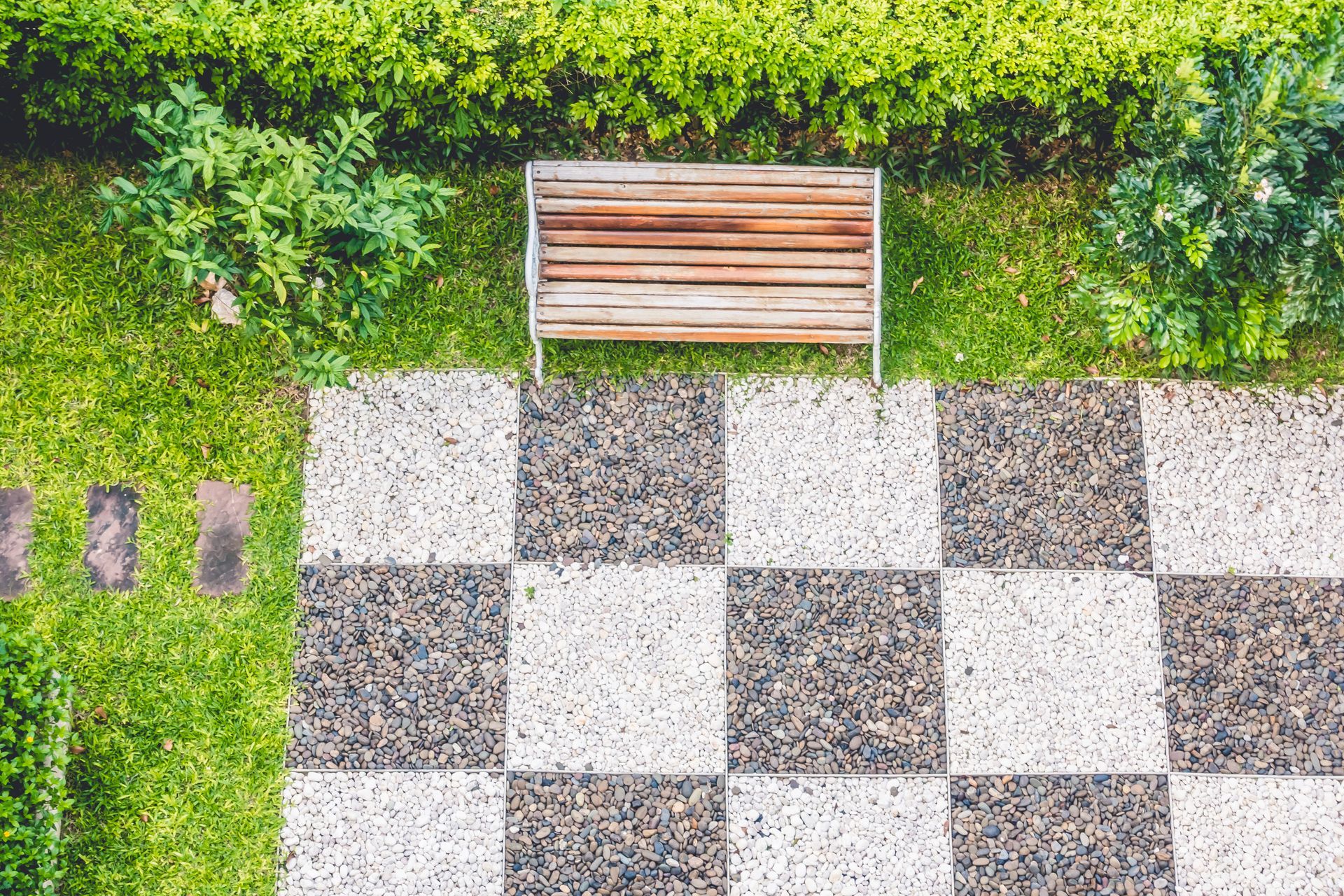 A wooden bench is sitting on a checkered walkway in a park.