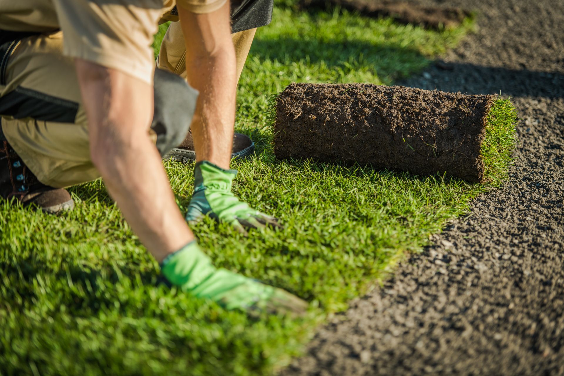 A man is rolling a roll of grass on the ground.