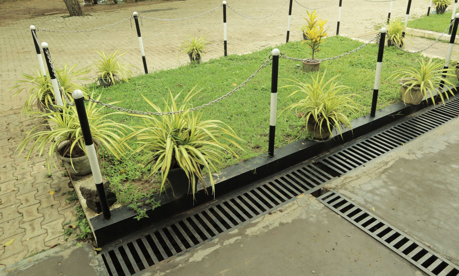 A garden with potted plants and a drain on the side of the road.