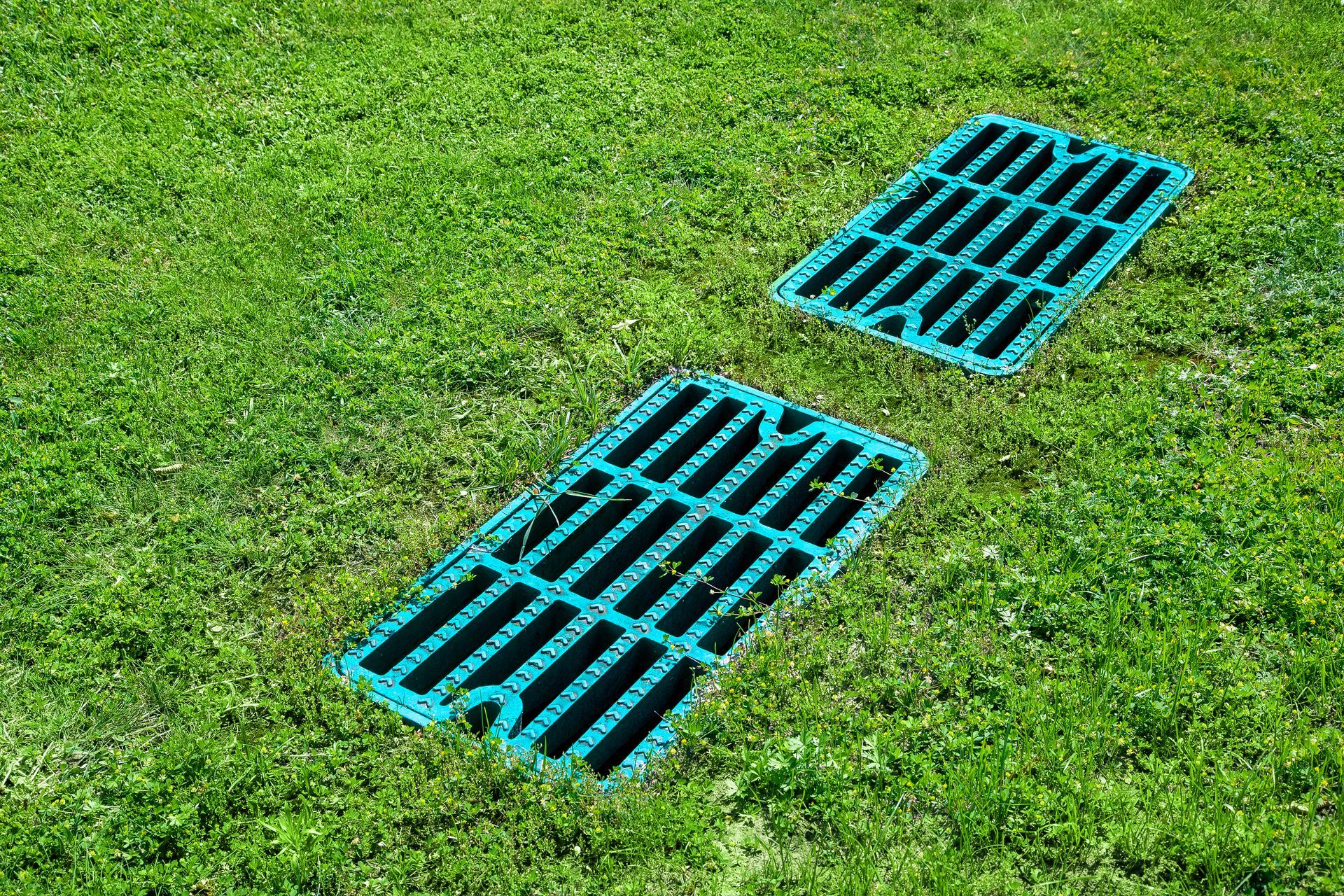 Two turquoise drainage grates set in green grass.