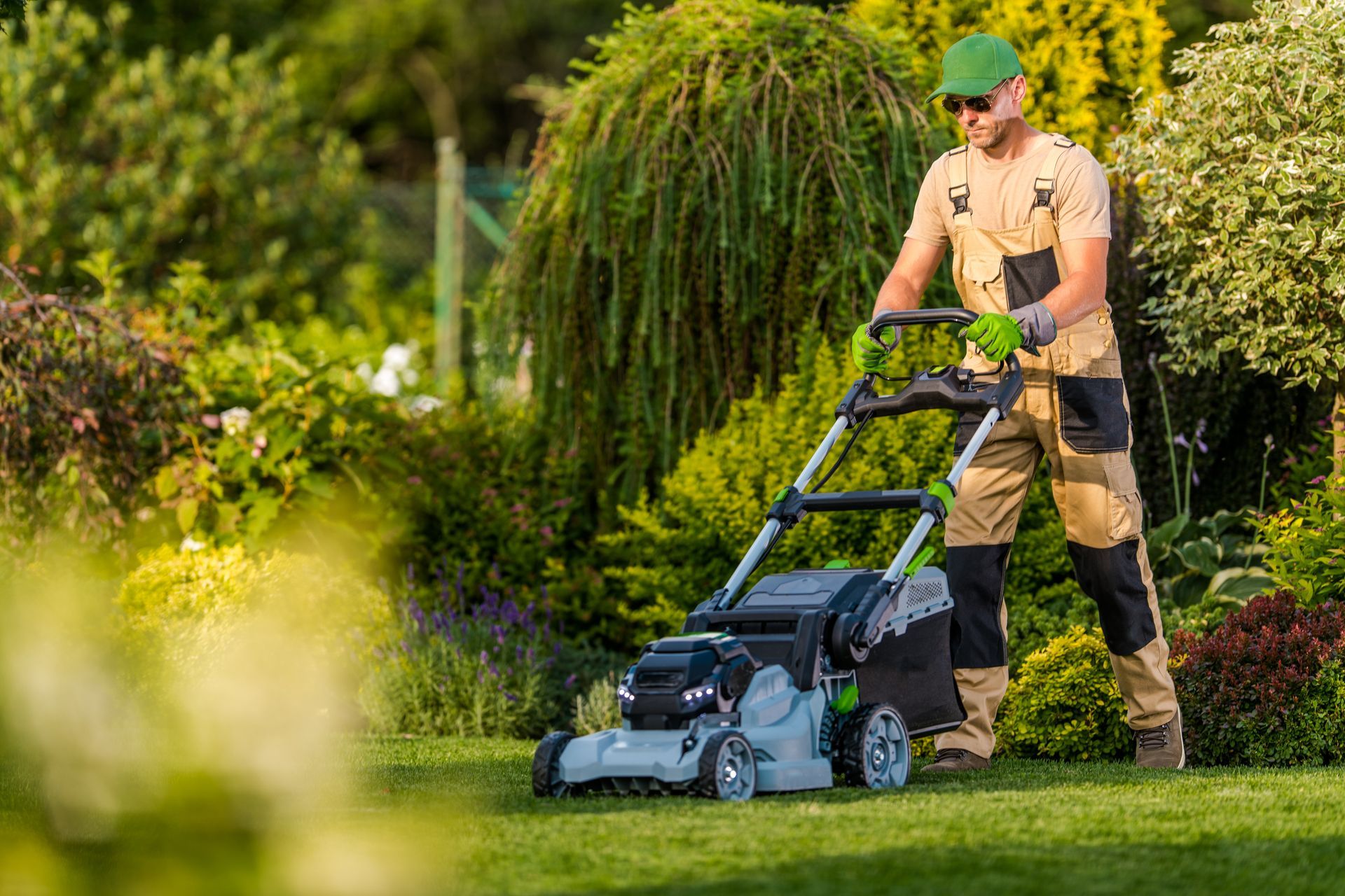 Man mowing a lawn with an electric lawnmower in a sunny garden.