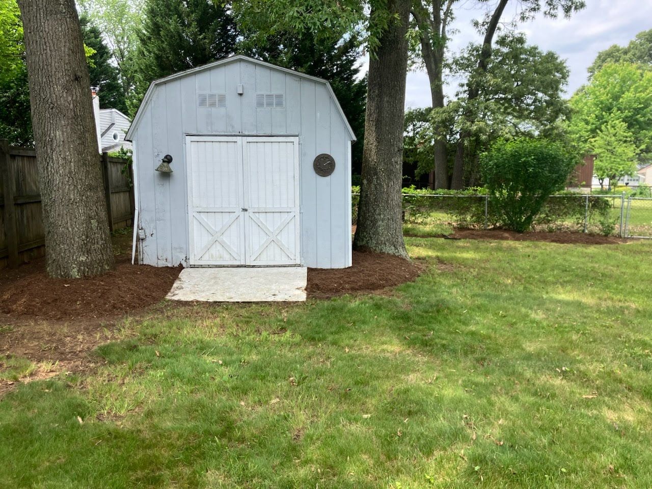 A white barn shed is sitting in the middle of a lush green yard.