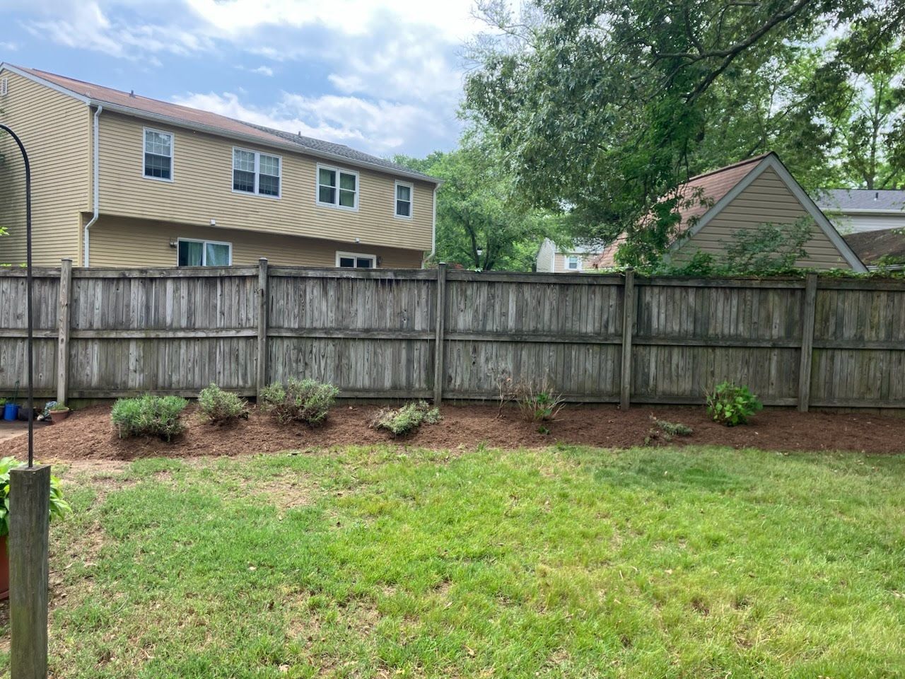 A backyard with a wooden fence and a house in the background.