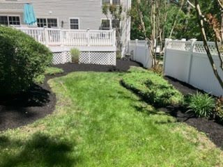 A lush green backyard with a white fence and a deck.