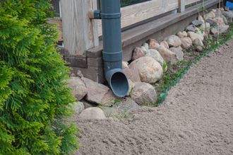 A drainpipe is sitting on a rocky sidewalk next to a fence.