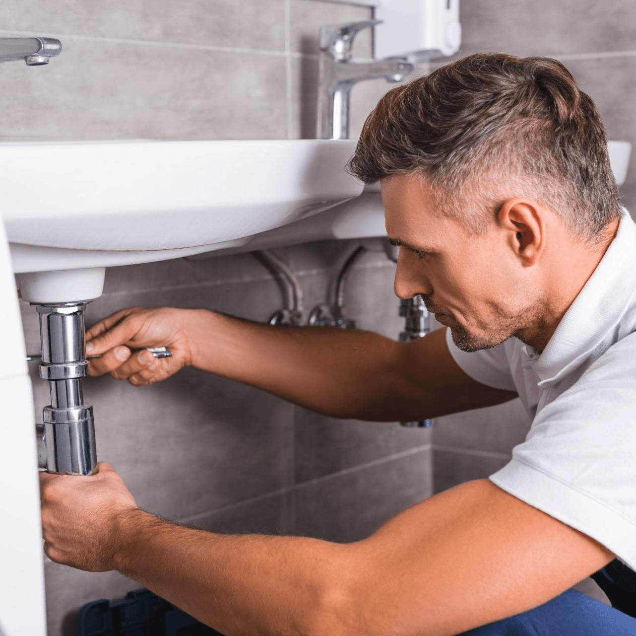 A man is fixing a sink in a bathroom.