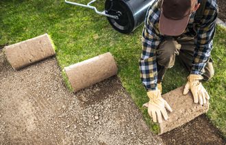 A man is rolling a roll of turf on a lawn.