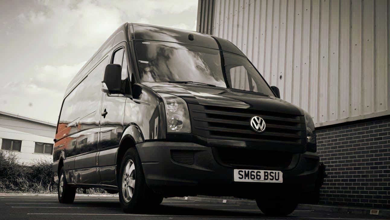 A black van is parked in front of a brick building.