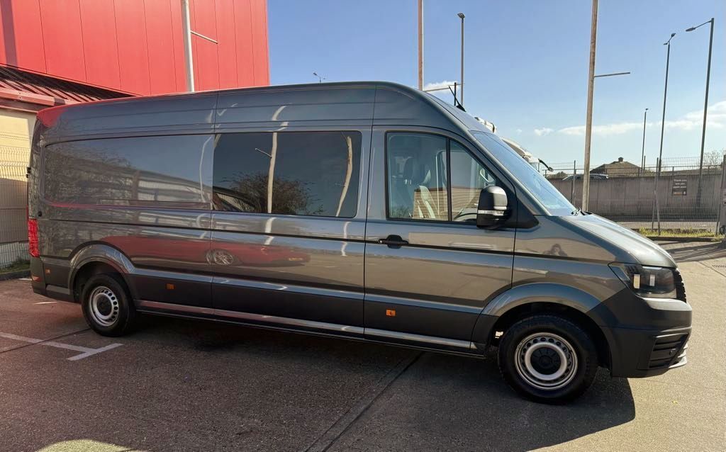 A gray van is parked in a parking lot in front of a red building.