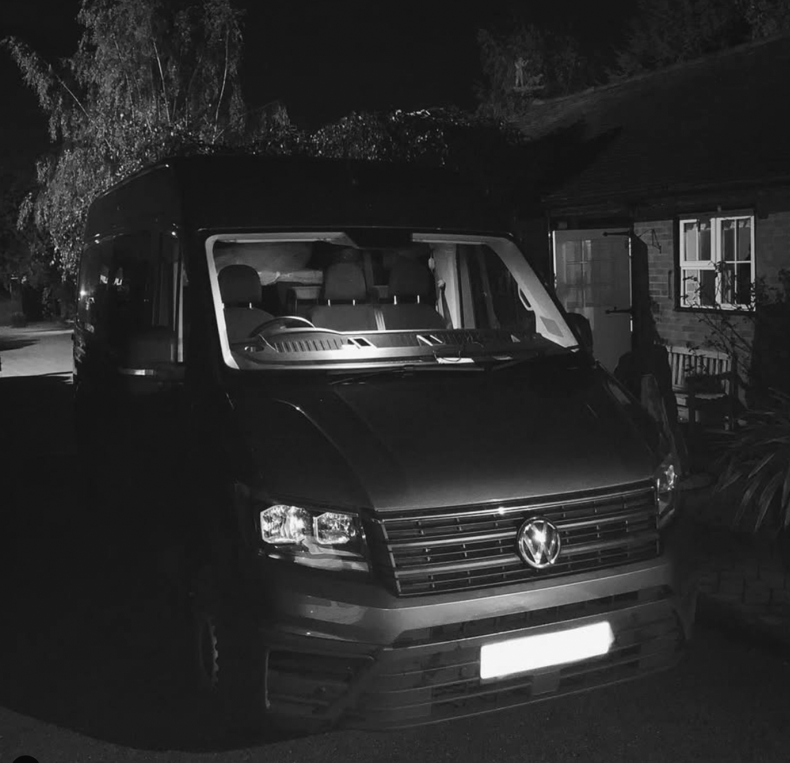A black and white photo of a van parked in front of a house