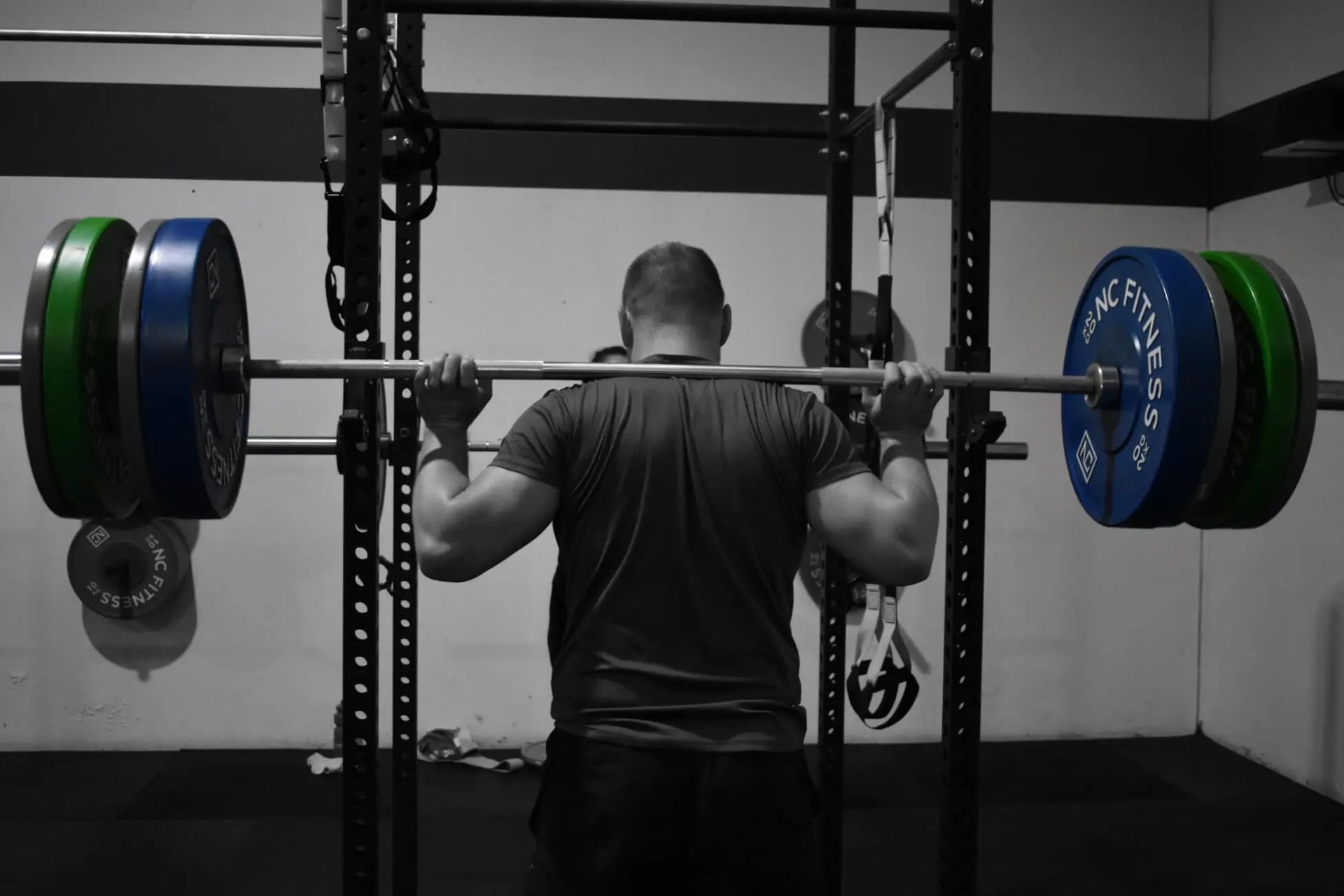 A man is squatting with a barbell in a gym.