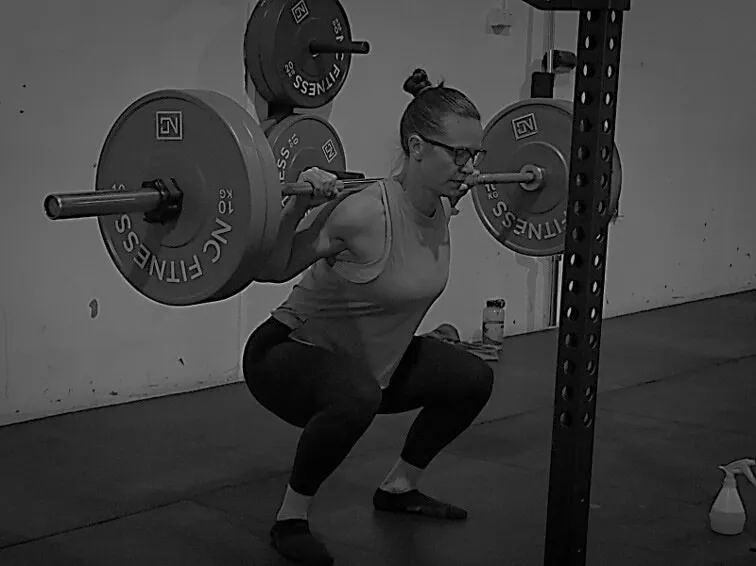 A woman is squatting with a barbell in a gym.