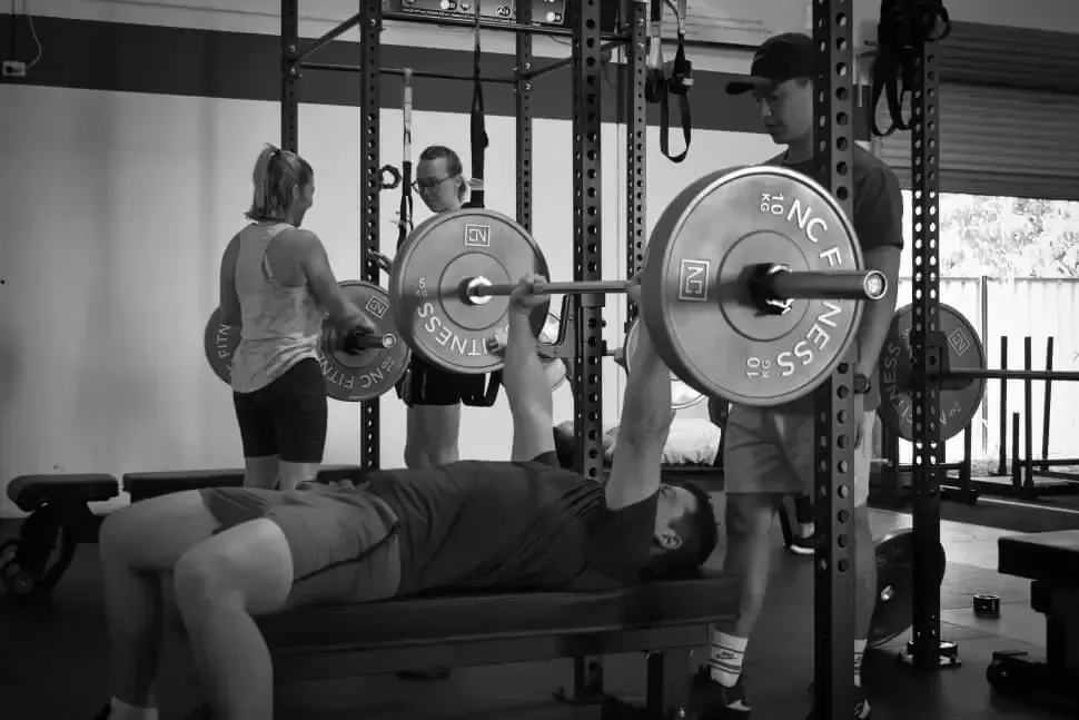 A man is lifting a barbell on a bench in a gym.